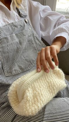 a woman wearing an apron and holding a knitted mitt in her hands while sitting on a couch