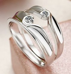 two white gold wedding rings with diamonds on each one, sitting on top of a pink cloth