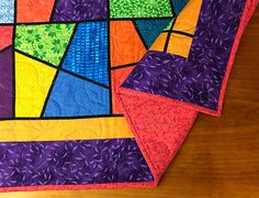 two colorful quilts sitting on top of a wooden table