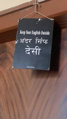 a black sign hanging from the side of a wooden door that says keep your english outside