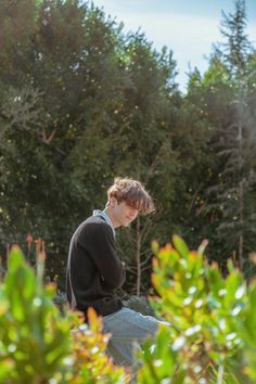 a young man sitting on top of a wooden bench in front of some bushes and trees