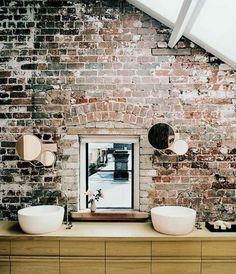 two white bowls are sitting on a wooden table in front of an exposed brick wall