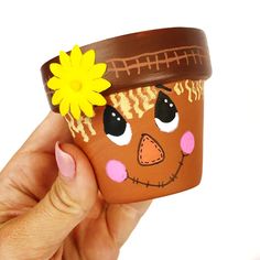 a hand holding a clay pot with a flower on it's head and painted face