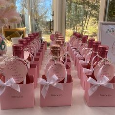 many pink boxes with white bows are on a table in front of a large window