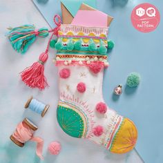 a colorful stocking with pom poms and thread spools next to it