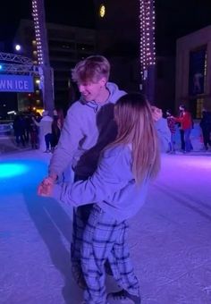 a man and woman skating on an ice rink at night with lights in the background