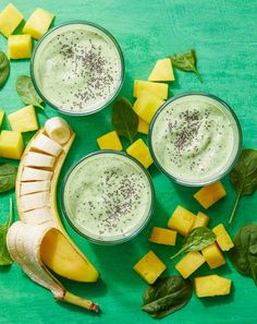 two glasses filled with green smoothie next to sliced bananas and spinach