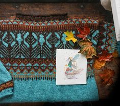 a knitted blanket with a card and some autumn leaves