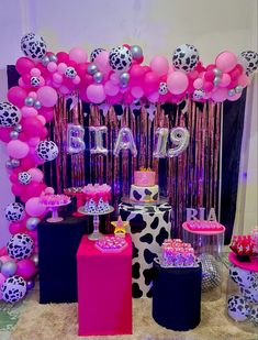 a table topped with lots of pink and black balloons next to a cake covered in confetti