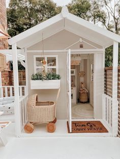 a small white dollhouse with a baby carriage in the door and potted plants