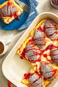 a pan filled with cake covered in powdered sugar next to a cup of tea