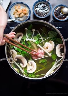 someone holding chopsticks over a pot of soup with mushrooms and other foods on the stove