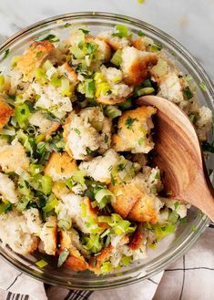 a bowl filled with stuffing and vegetables on top of a white table cloth next to a wooden spoon