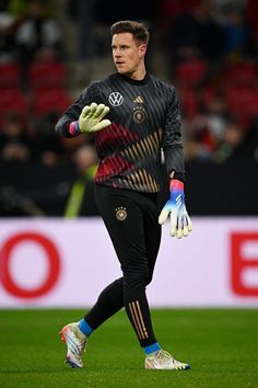 a soccer player in black and red uniform holding a ball on a field with people watching