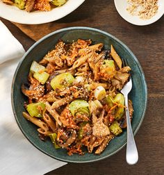 a bowl filled with stir fry vegetables on top of a wooden table next to two plates of food