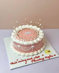 a pink and white birthday cake with an analog clock on it's side, sitting on top of a card board