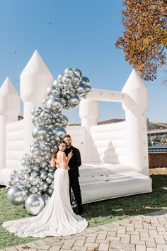 a bride and groom standing in front of an inflatable bed with silver balloons