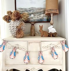 an old dresser with some bunny decorations on it and a painting in the corner behind it