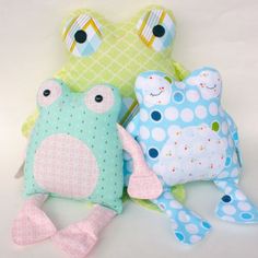 three stuffed animals sitting next to each other on a white surface, one is green and the other is blue