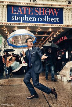 a man in a suit and tie is holding an umbrella while walking down the street