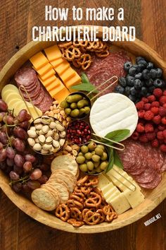 a wooden bowl filled with different types of cheese and crackers, grapes, nuts, meats, and pretzels