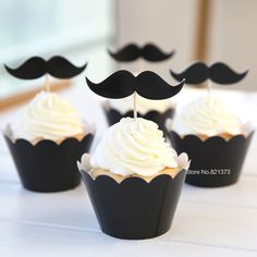 cupcakes with white frosting and black moustaches are on the table