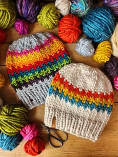 multicolored knitted beanie hat next to scissors and balls of yarn on wooden surface