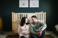 a man and woman sitting next to each other in front of a baby crib