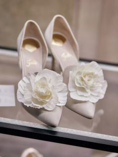 two pairs of white shoes with flowers on the toes and one pair is sitting on a glass table