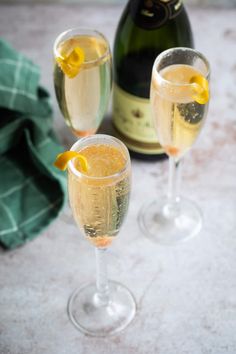 two champagne flutes with lemon wedges in them next to a bottle of sparkling wine