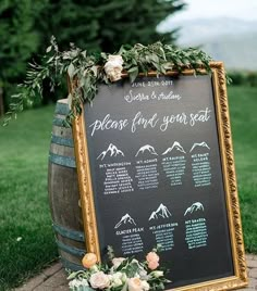 a chalkboard sign with flowers and greenery on it sitting in front of a barrel