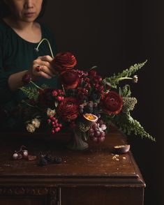 a woman arranging flowers on top of a wooden table