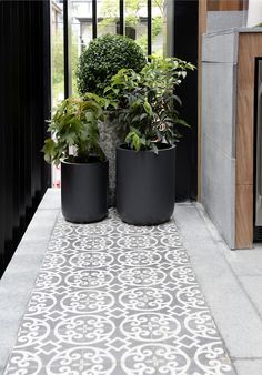 two black planters sitting on the side of a building next to a sidewalk with potted plants