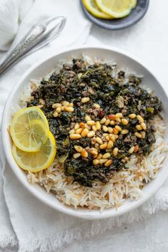 a white plate topped with rice and spinach next to lemon wedges on a table