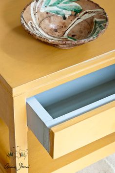 a bowl sitting on top of a yellow table next to a drawer with drawers underneath it