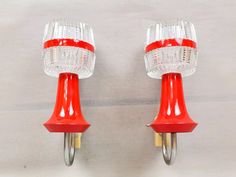 two red and clear glass wall lights on a white background, one is plugged into the other