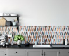 a kitchen with grey cabinets and colorful wallpaper on the back splash, along with a white sink