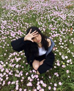 a woman is sitting in the middle of a field with pink flowers and holding her hands to her head