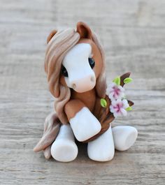 a small toy horse sitting on top of a wooden table with flowers in it's mouth