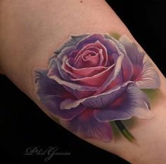 a pink rose tattoo on the left side of the arm, with purple petals and green leaves