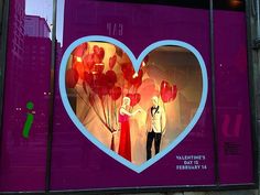 there is a window display with balloons in the shape of a heart and two people holding hands