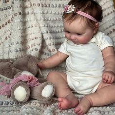 a baby sitting on a blanket next to a teddy bear