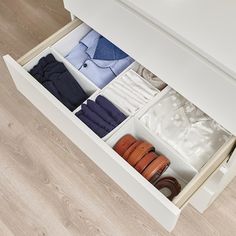 an open drawer with clothes and shoes in it on the floor next to a wooden floor