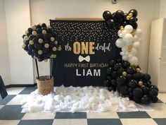 a black and gold first birthday party with balloons, streamers, and an arch