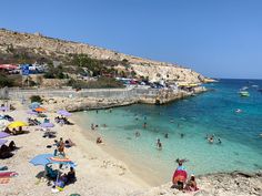 many people are on the beach and in the water near some cliffs, with boats