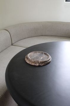 a round black table with a wooden plate on it's center piece in front of a white couch