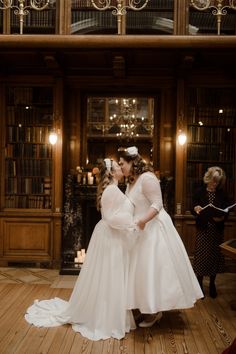 two brides kissing in front of a bookcase with candles on the floor and bookshelves behind them