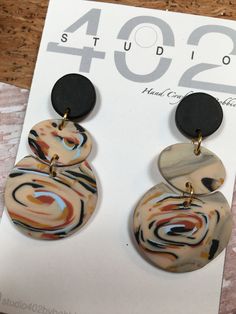 Handmade, Polymer Clay, statement earrings, made in a beautiful marble swirl of southwest colors, topped with a black circle, these dangle style earrings are finished in gold. Studio 402 Earrings are handmade in Lincoln, Nebraska by my Dad and I. Our earrings are made of light weight and durable polymer clay. Each set is unique and subject to minor variations or slight imperfections. Earring posts and backs are nickel free for all of the sensitive ears out there! Handle with care. Clean gently with a damp cloth. Rubbing alcohol may be used to clean. We recommend storing these in a dry, room temperature environment. Do not wear in water. Whimsical, fun, and attractive! be prepared for compliments ;) If you have any questions or would like a custom order: message us here or on our Instagram Artsy Black Earrings With Ear Wire, Artsy Black Dangle Earrings, Artsy Black Drop Earrings, Black Artsy Drop Earrings, Southwest Colors, Unique Marble, Clay Things, Lincoln Nebraska, Black Circle