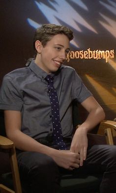 a young man sitting in a chair wearing a tie