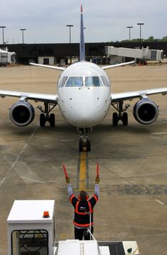 a man standing in front of an airplane on the tarmac with his hands up